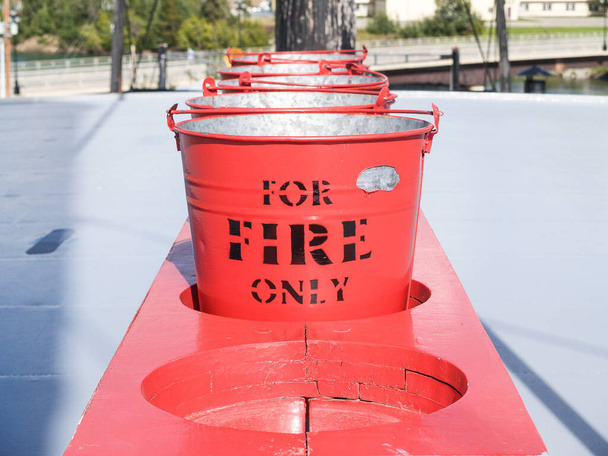 Row of red buckets in rack with sign for fire only for emergency. - Foto, immagini