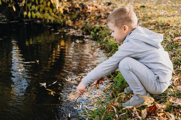 Lonely boy admiring the beauty of the autumn lake in the city park. Boy playing outside - imitate fishing at a lake. Autumn forest. - Foto, Imagen