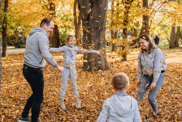 Young family of four members rejoicing in a forest throwing leaves in the air on an autumns day. Fall foliage. Family outdoor fun in autumn. Toddler or - Фото, изображение