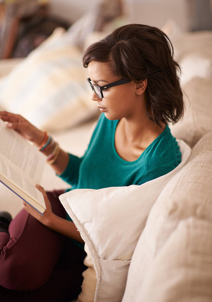 Taking a break with the latest bestseller. a young woman reading a book on the sofa at home - Foto, Imagen