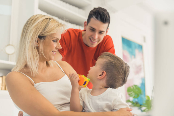 Busy morning of loving family of three. Millennial married caucasian couple and their excited brown-haired toddler boy talking to each other and smiling. Kitchen interior. High quality photo - Foto, Bild