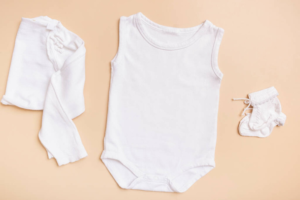 White baby bodysuit mockup for logo, text or design on beige background with clothes top view. - 写真・画像