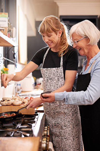 Just a dash. a senior woman and a younger woman cooking together - Foto, Imagen