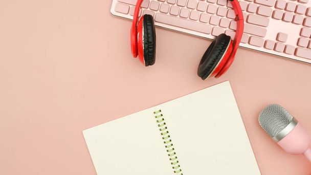 Red wireless headphones, microphone and notepad on pink background. Technology and audio equipment concept. - Фото, зображення
