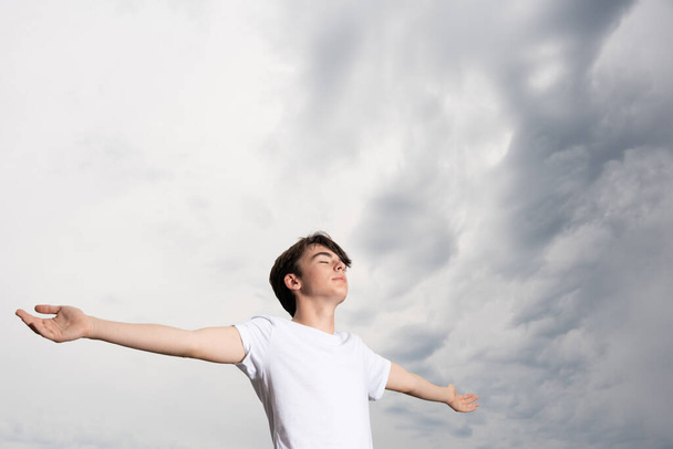 Teenager boy meditating and breathing in nature with dramatic stormy sky. Guy praying for rain. - Photo, image