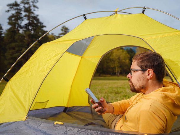 trip to Caucasus mountains, Arkhyz, Teberdinsky reserve. Man traveler relaxing in mountains in tent camping outdoor , uses app on smartphone. Travel adventure lifestyle concept hiking active vacations - Photo, image