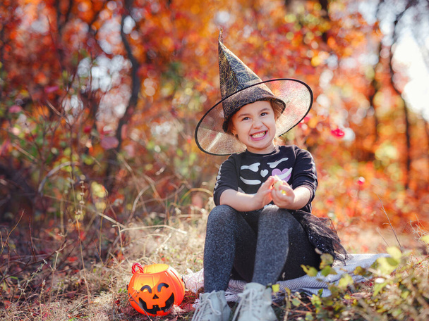 Young girl in black costume goes trick or treating. Little witch, Kids with jack-o-lantern. Children with candy bucket in fall forest. Happy Halloween. - Zdjęcie, obraz
