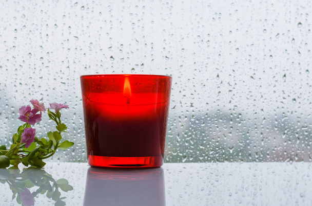 Burning aroma candle puts near by window with small tree and flowers that have rain drop in monsoon season. Zen and relax concept. - Photo, Image
