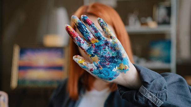 Female calm red-haired girl artist lady Caucasian 30s woman painter designer holding hand in front stop gesture not no gesture showing dirty in acrylic paint palms looking at camera in art studio - Fotografie, Obrázek