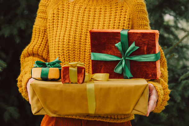 Woman in yellow sweater with fabric eco friendly Christmas gift boxes on Christmas tree background - Foto, Imagem