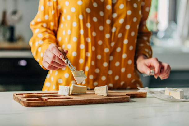 Female in yellow polka dot shirt with a cheese on table in kitchen - Fotó, kép