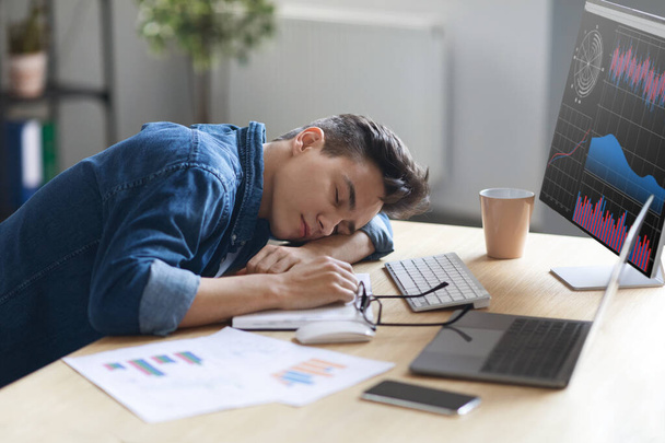 Portrait Of Tired Young Male Employee Sleeping At Work, Exhausted Millennial Guy Resting At Desk Near Monitor With Financial Analysis, Fatigued Man Napping In The End Of Hard Working Day - Photo, Image