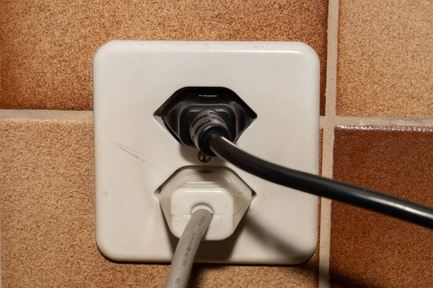 Vaduz, Liechtenstein, September 6, 2022 Electric power plug put in a socket to generate electricity in an apartment - Foto, afbeelding
