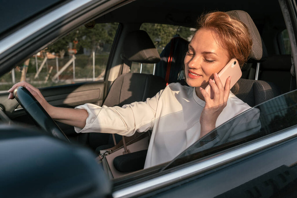 Lächelnde selbstbewusste Geschäftsfrau im Handy-Gespräch am Steuer eines neuen bequemen Autos  - Foto, Bild