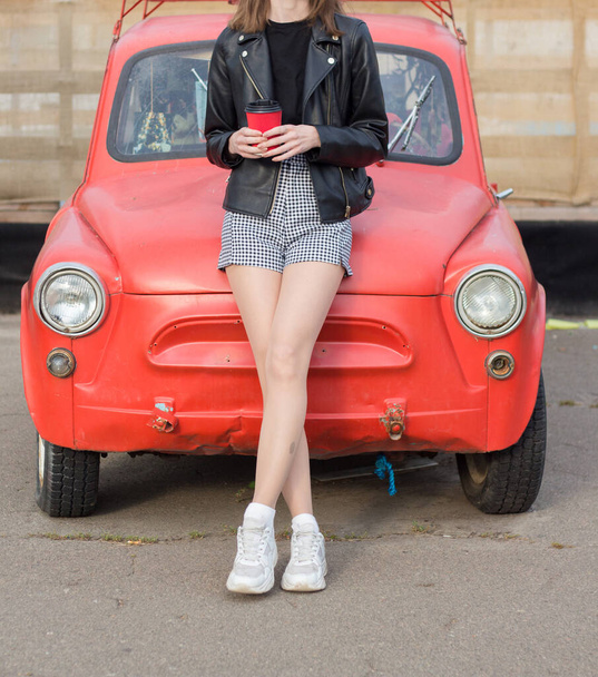 Девушка с кофе стоит перед старой красной машиной - Фото, изображение
