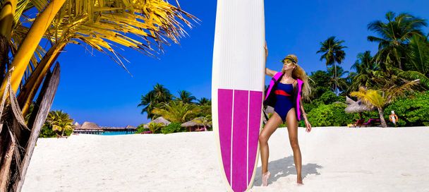Beautiful sexy tanned woman in bikini is holding surfboard at Maldives sand beach. Maldives landscape. Girl with surfboard. Surfer girl. Luxury travel. Lifestyle. Tourism. Sport and recreation. - Photo, image