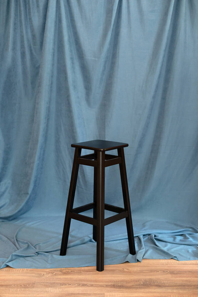 zwart minimalistische houten stoel tegen blauwe achtergrond. Onderwerp modern interieur en design meubels in de kamer. Hoge kruk in loft stijl. Retro Bar stoel. Vintage houten stoel. Lange staande tafel. - Foto, afbeelding