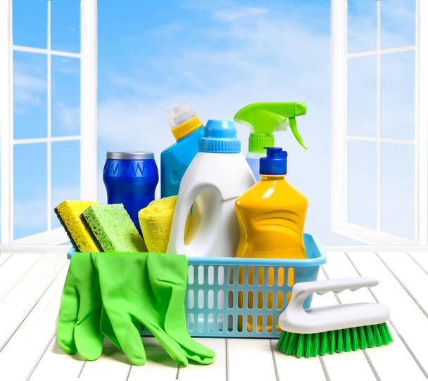 Household cleaning supplies in plastic basket on the white table over the open window and sky background. Copy space - Photo, image