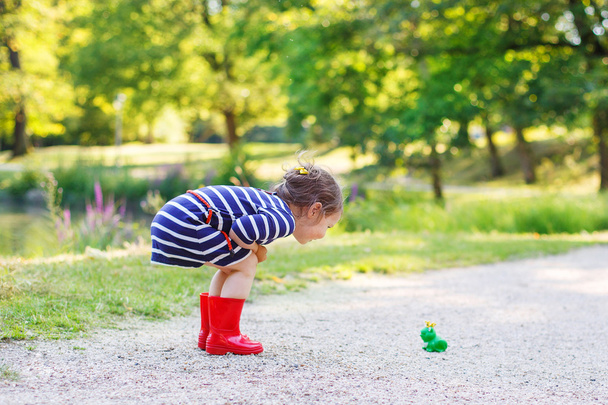 Hermosa niña en botas de lluvia rojas jugando con rana de goma
 - Foto, imagen