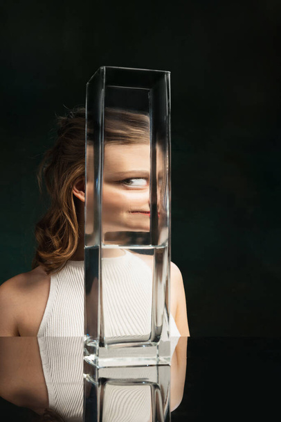 Weird look. Creative art photography. Young girls face through glass vase over dark green background. Object distortion, optical illusion. Minimalistic contemporary art. Poster - Fotoğraf, Görsel