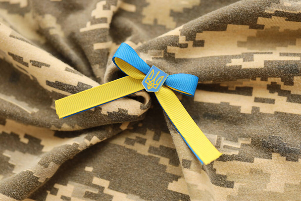 TERNOPIL, UKRAINE - SEPTEMBER 2, 2022 Ribbon with Ukrainian Coat of Arms and national flag colors on army camouflage uniform cloth - Foto, Imagen