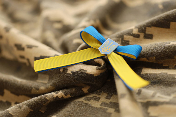 TERNOPIL, UKRAINE - SEPTEMBER 2, 2022 Ribbon with Ukrainian Coat of Arms and national flag colors on army camouflage uniform cloth - Foto, afbeelding