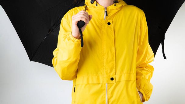 A woman in a yellow raincoat holds a black umbrella on a white background. High quality photo - Foto, imagen