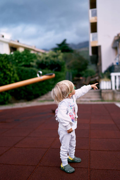 Little girl in a tracksuit points her finger at the house. High quality photo - Valokuva, kuva