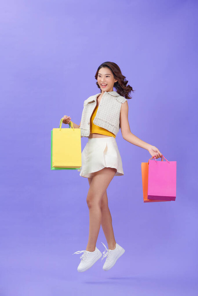Beautiful young woman with paper shopping bags on a purple background - Фото, изображение