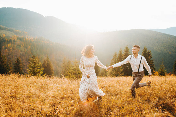 A boho wedding in the mountains. Happy newlyweds running at sunset - Zdjęcie, obraz