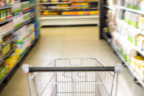 Shopping cart on aisle amidst products in supermarket - Foto, imagen