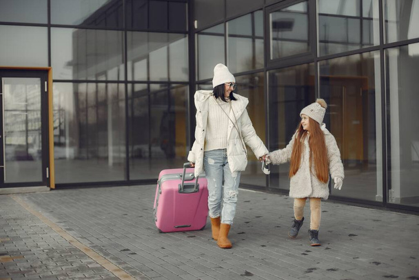 Mother and daughter come back from vacation. Brunette woman and girl with a luggage going from airport terminal. Mother and daughter wearing warm clothes. - Foto, Bild