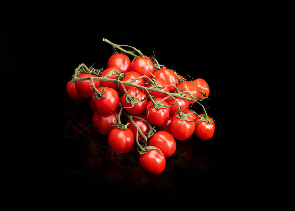 Ripe cherry tomatoes on stems, branches, top view. Group of small red tomatoes on green twigs, on black background. - Photo, Image