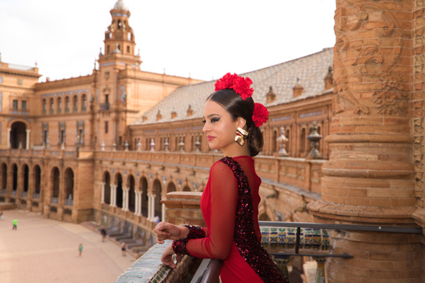 Beautiful teenage woman dancing flamenco on the balcony of a square in Seville. She wears a red dress with ruffles with a lot of art. Flamenco cultural heritage of humanity. - Photo, Image