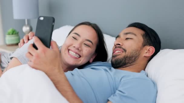 Happy interracial couple, bed and phone scroll of a Asian woman and Arab man in a bedroom. In love people at home relax at home looking at mobile internet, web and social media app content at a house. - Footage, Video