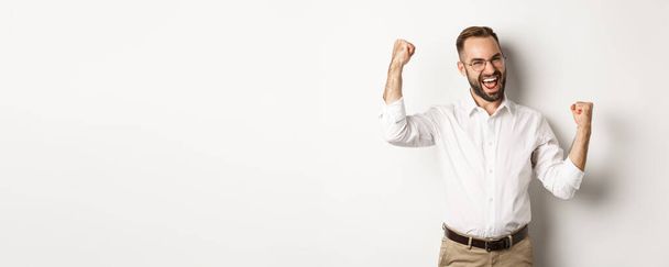 Successful businessman rejoicing, raising hands up and celebrating victory, winning something, standing over white background. - Photo, Image
