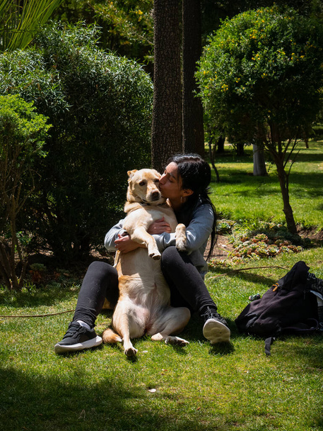 Peruvian Woman Sitting on the Grass, Hugging a Yellow Mongrel Dog and Surrounded by Lots of Nature - Foto, afbeelding