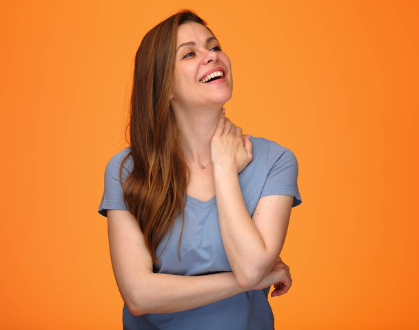 Smiling happy young woman in blue shirt touchung her neck and looking up isolated portrait on orange background. - Фото, изображение