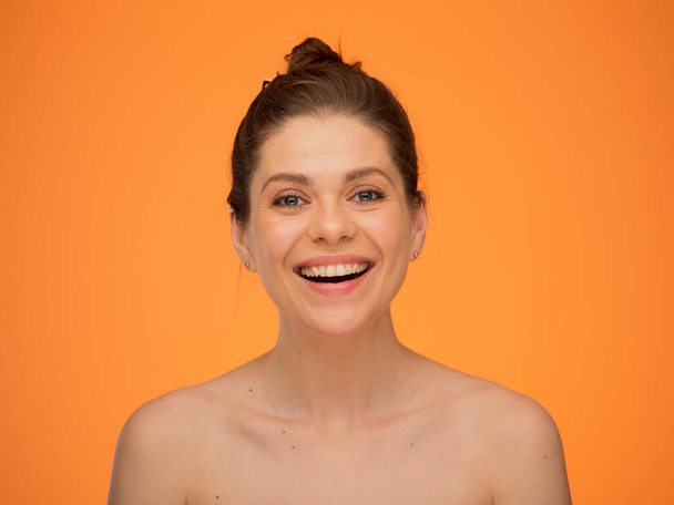 Face close up portrait of smiling woman with naked shoulders isolated on orange yellow background. - Фото, зображення