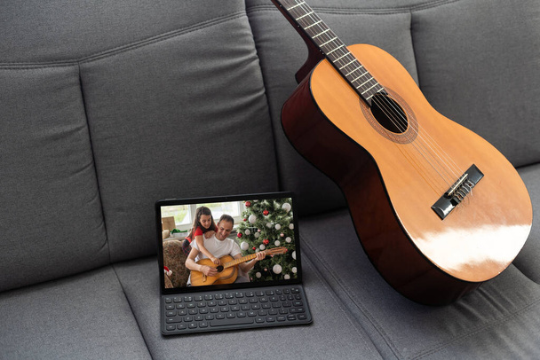 Acoustic guitar and digital tablet on a couch at cozy home background. Online music lessons, learning playing or writing songs and hobby concept. - Фото, изображение