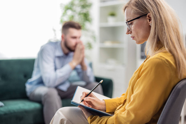 Woman medical doctor psychologist making notes while listening to male patient, talking about problem and it solution, mental healthcare concept - Photo, image