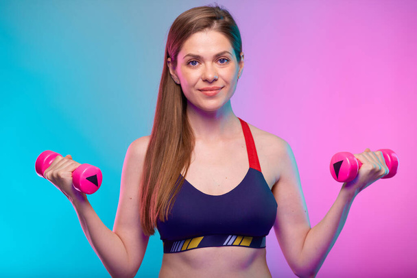 sporty woman with long hair dressed in fitness bra doing exercise with pink dumbbells. Female portrait isolated on neon color background. - Fotografie, Obrázek