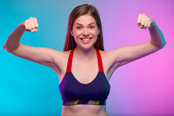 Power muscle concept with sporty woman in fitness sportswear flexes her arm. Female fitness portrait isolated on neon multicolor background. - Fotó, kép