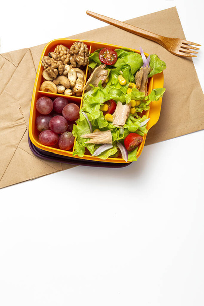 Healthy Food in Plastic container ready to eat with homemade lettuce salad with tomato, onion, corn, tuna, roga grapes, walnuts and cashews in paper bag fro, above. Take away concept - Фото, изображение