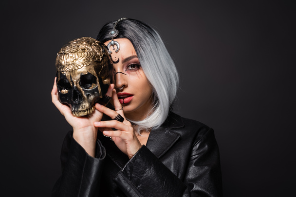 young witch style woman with ash blonde hair obscuring face with spooky golden skull isolated on black - Valokuva, kuva