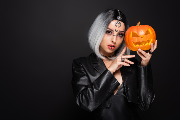 ash blonde woman in witch costume holding jack o lantern isolated on black - Fotoğraf, Görsel