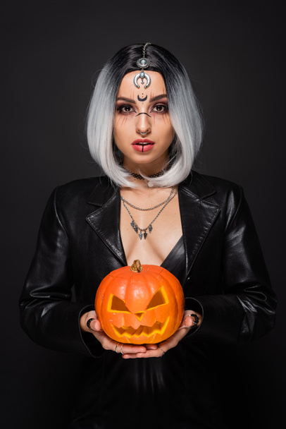 sexy woman in witch halloween makeup holding jack o lantern and looking at camera isolated on black - Fotoğraf, Görsel