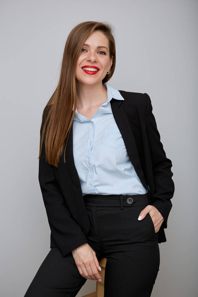 Smiling woman in black business suit sitting on tall stool. Young business woman isolated portrait. - Fotografie, Obrázek