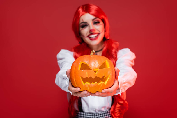 smiling blurred woman in halloween makeup holding jack o lantern isolated on red - Foto, Imagen