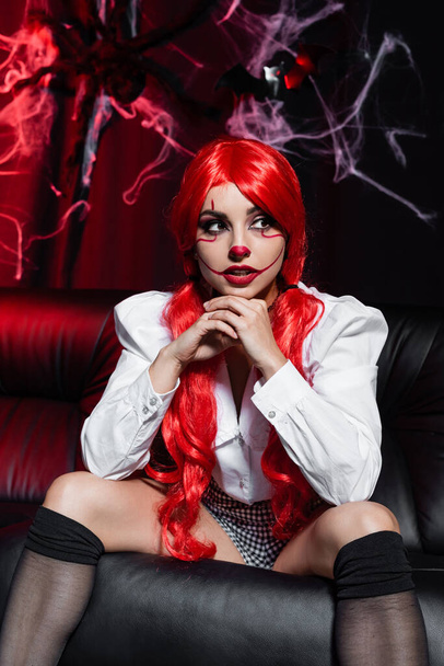σέξι κοκκινομάλλα γυναίκα με αποκριάτικο μακιγιάζ κάθεται σε σκούρο φόντο κοντά Spiderweb - Φωτογραφία, εικόνα